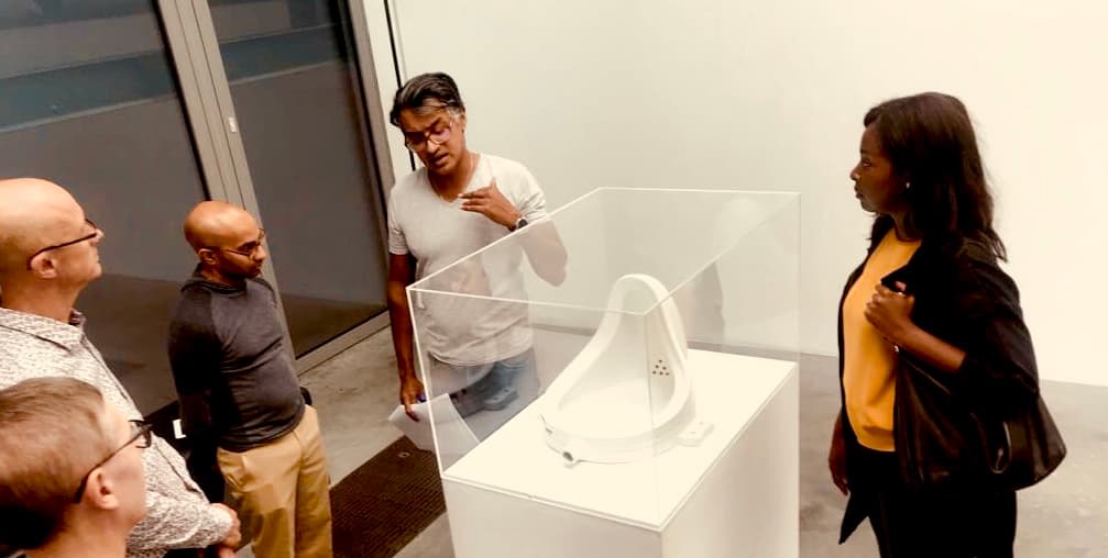 Jana Manuelpillai leading a guided gallery tour, discussing Duchamp's Fountain with visitors in a London gallery